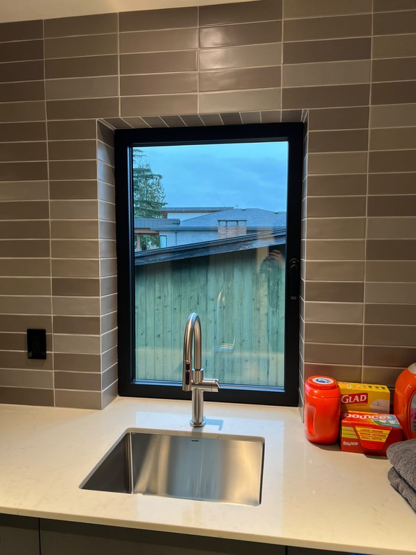 Black-framed window set into a tiled wall above a sink
